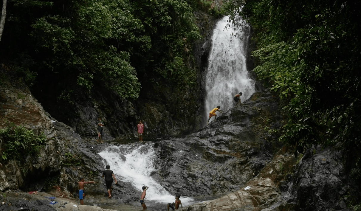 local filipino kids crossing stone bridge in front of the Hicming falls waterfall in catanduanes province philippines